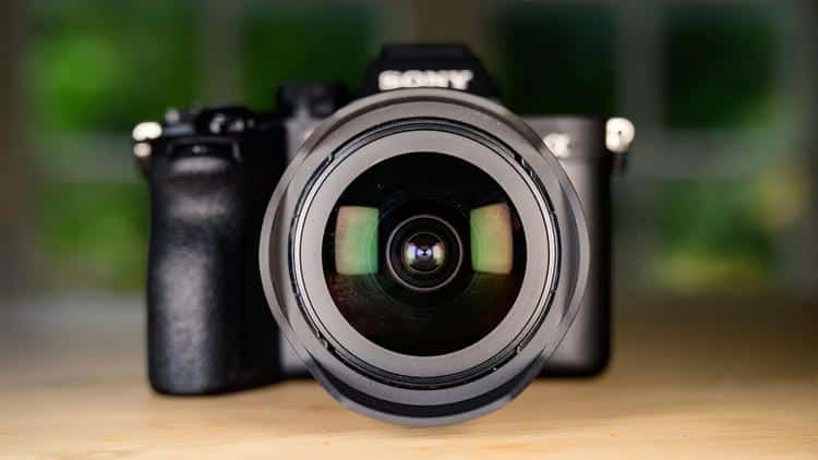 Крупный план фронтальной линзы объектива Sony FE 135mm f/1.8 GM на камере Sony с диаметром светофильтра 82 мм и радужными бликами антибликового просветления Nano AR.